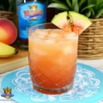 Tall glass of peach cocktail with fresh peach slices and mint by a tropical beach