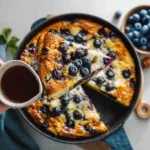 Golden blueberry buttermilk pancake casserole baked in a white dish, topped with syrup