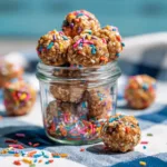 A rustic board filled with colorful Monster Cookie Energy Balls made of oats, M&Ms, chocolate chips, and peanut butter.